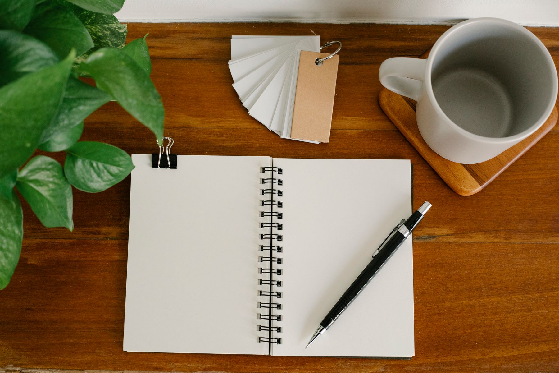 Carnet spiral, stylo noir, tasse de café et plante verte sur bureau en bois