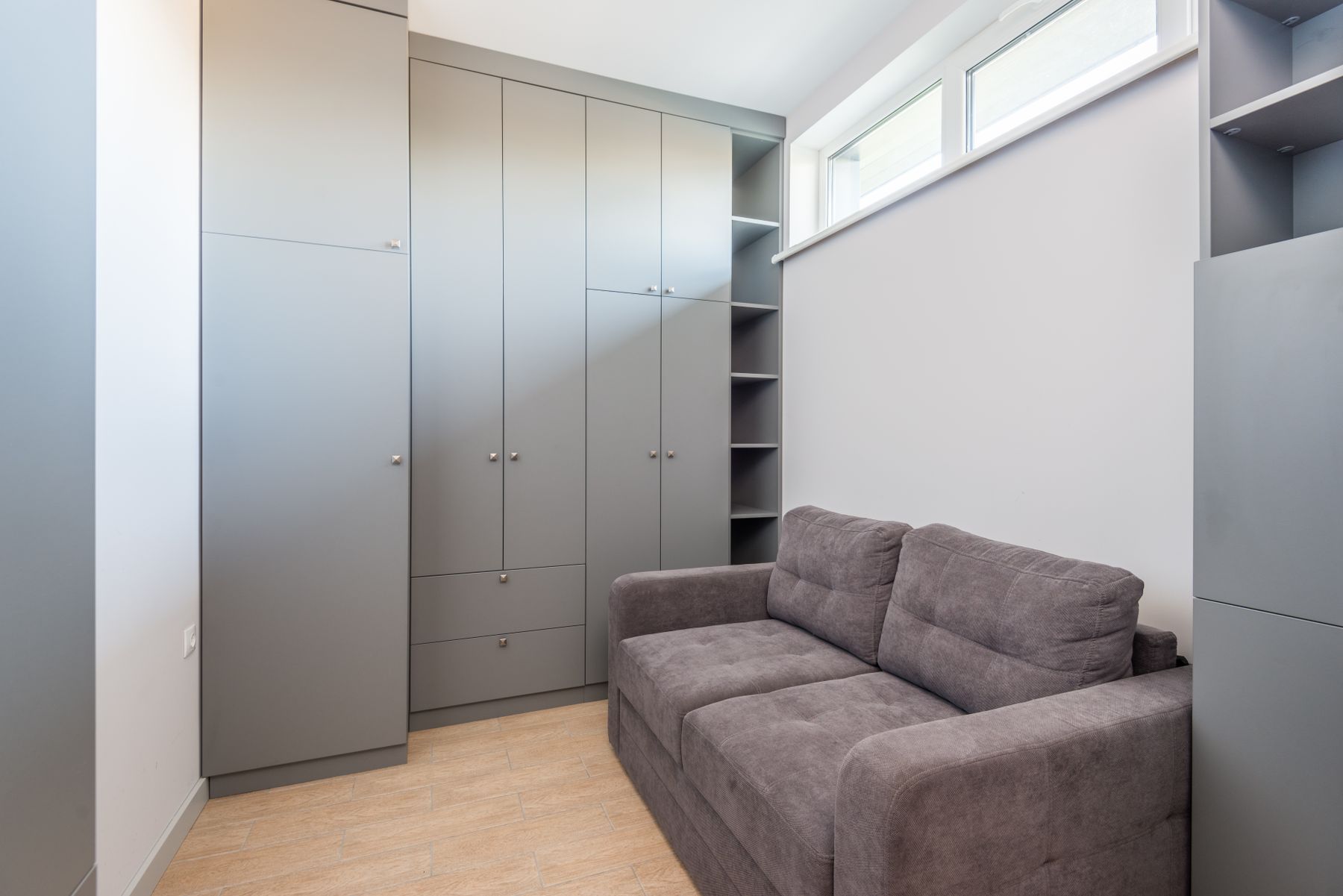 Petit appartement lumineux avec canapé gris, escalier blanc et rangements intégrés